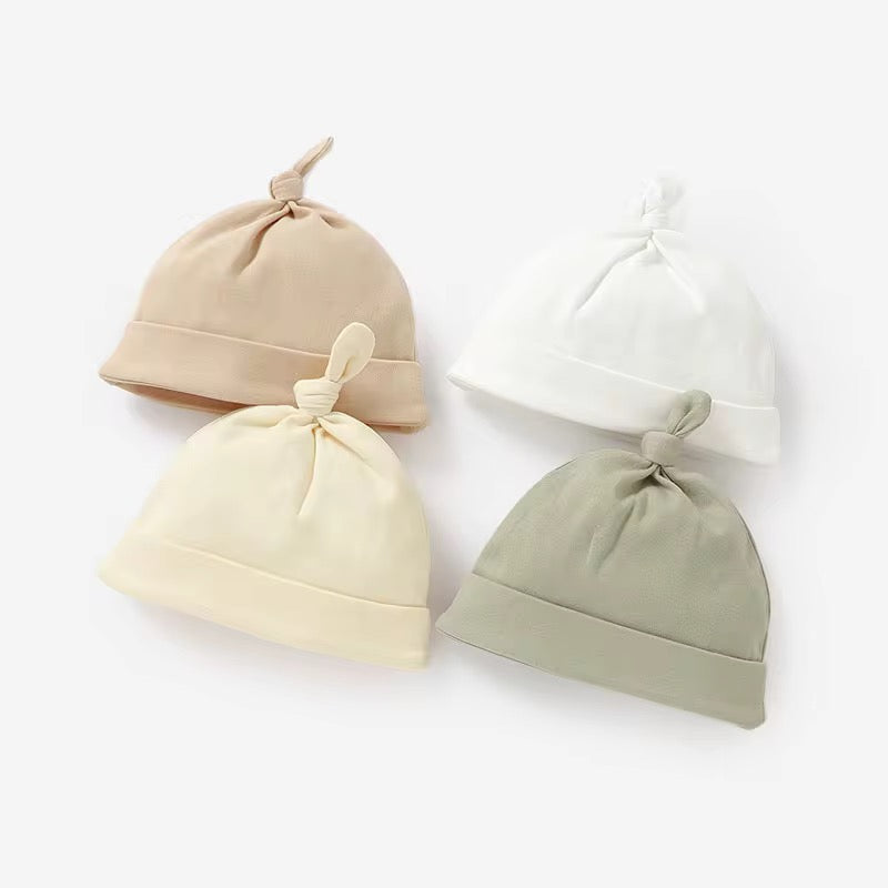 Four baby hats in beige, cream, and green on a white background