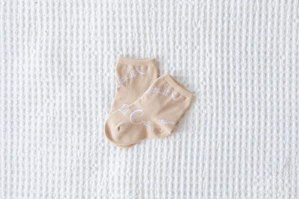 Pair of kids beige socks with text on a textured white background