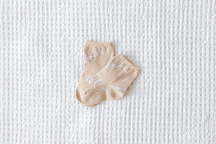 Pair of kids beige socks with text on a textured white background