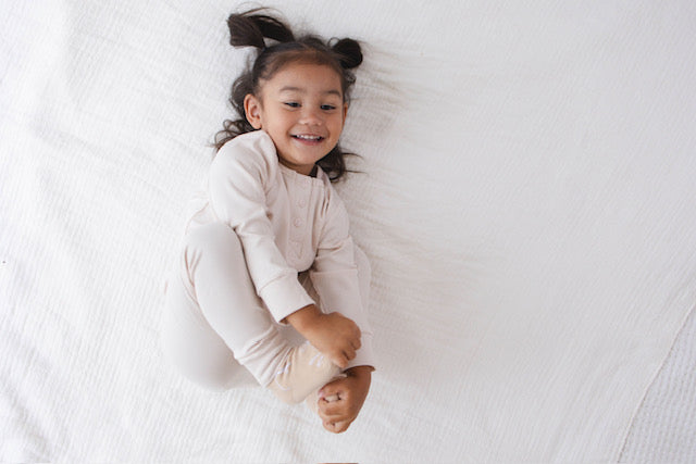 Child lying on a white bedspread, wearing a light-colored outfit.