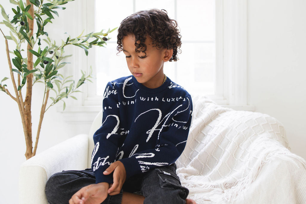 Child wearing a navy blue sweater with white text sitting on a white couch.